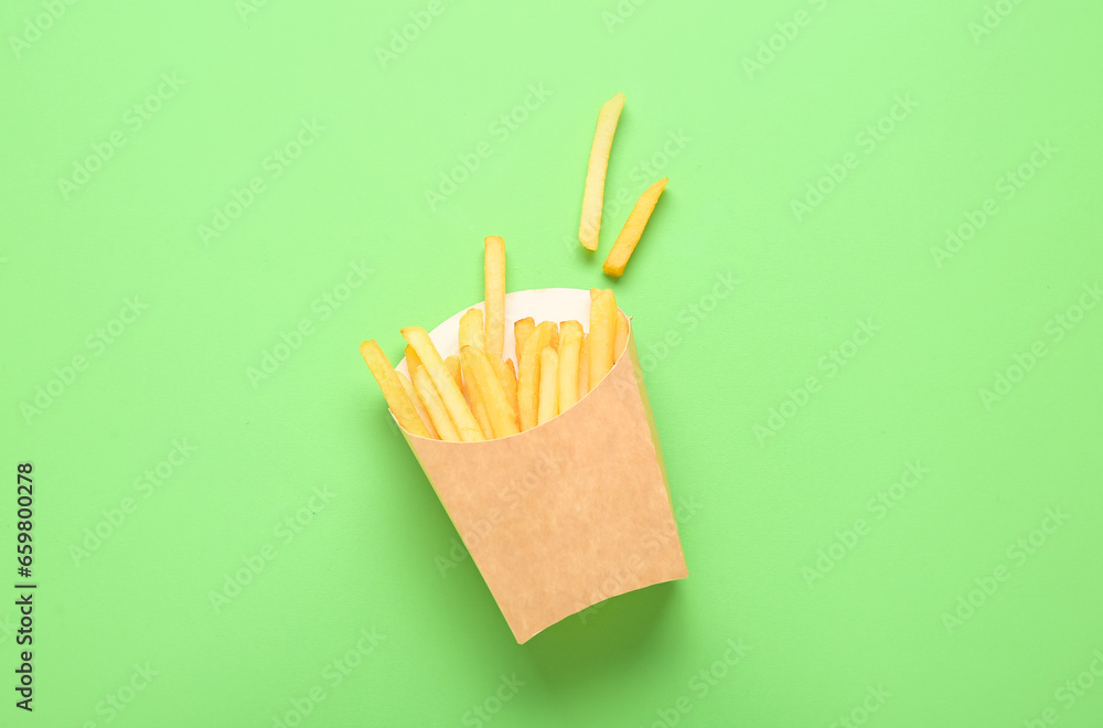 Paper box with delicious french fries on green background