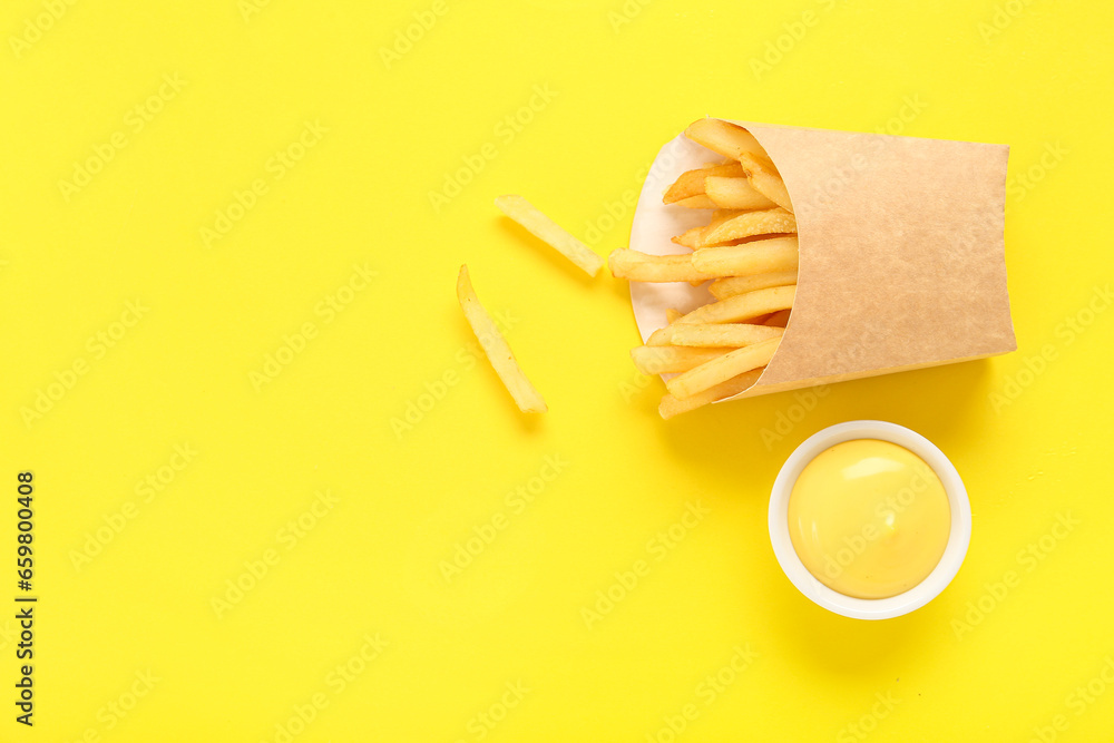 Paper box with delicious french fries and bowl of mayonnaise on yellow background