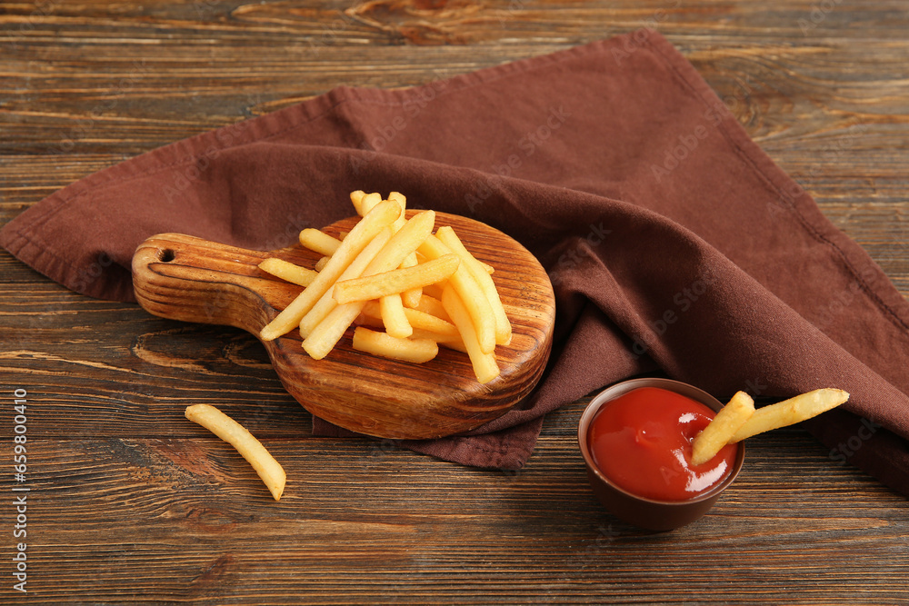 Board with tasty french fries and bowl of ketchup on brown wooden background