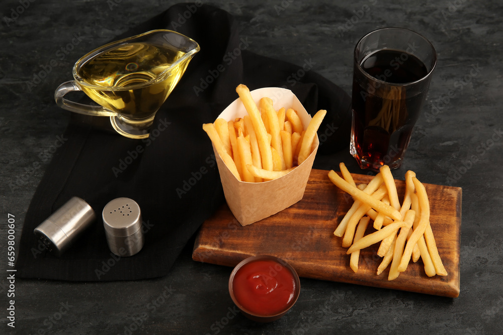 Board with tasty french fries, cola, bowl of ketchup and spices on black background