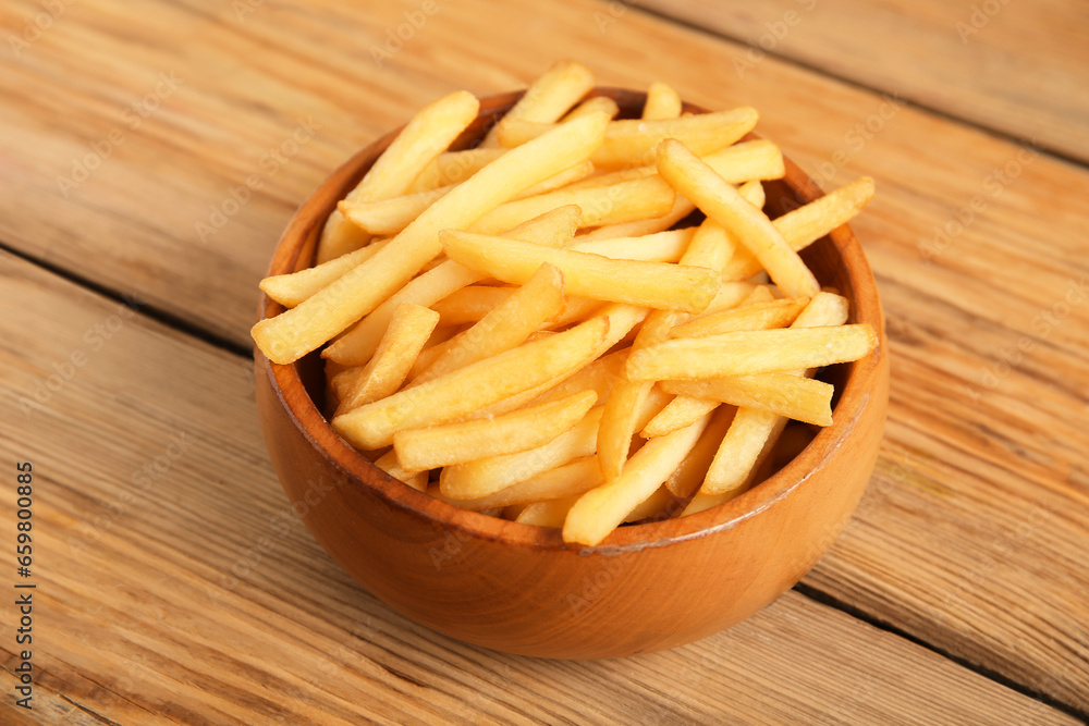 Bowl with tasty french fries on brown wooden background