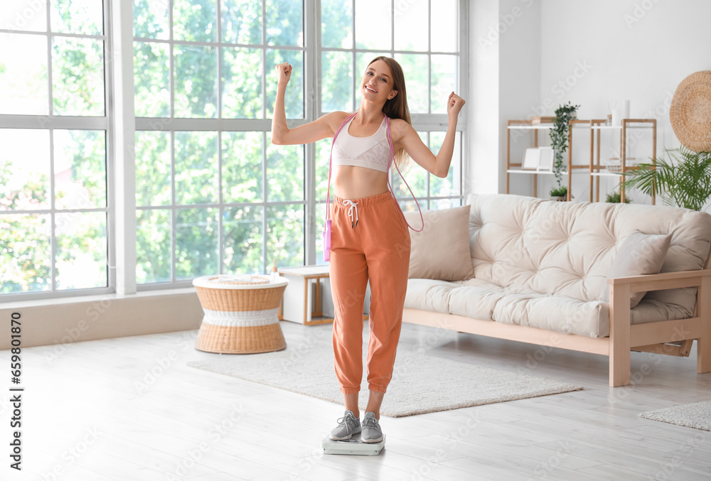 Beautiful young woman with skipping rope and scales in living room. Weight loss concept