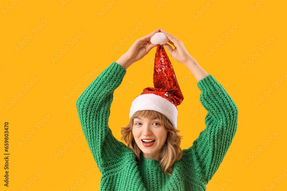 Young woman in Santa hat on yellow background