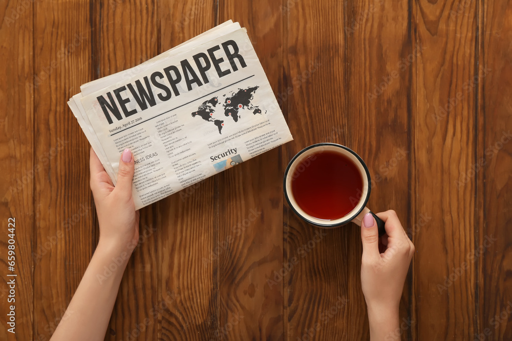 Woman with cup of tea reading morning newspaper on wooden background