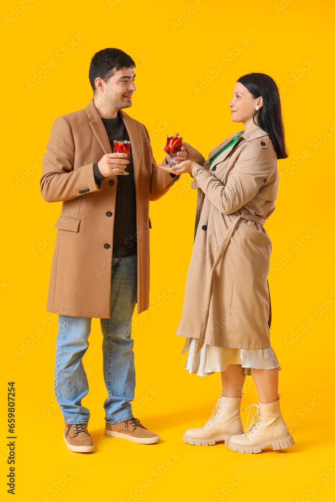 Young couple with glasses of mulled wine on yellow background