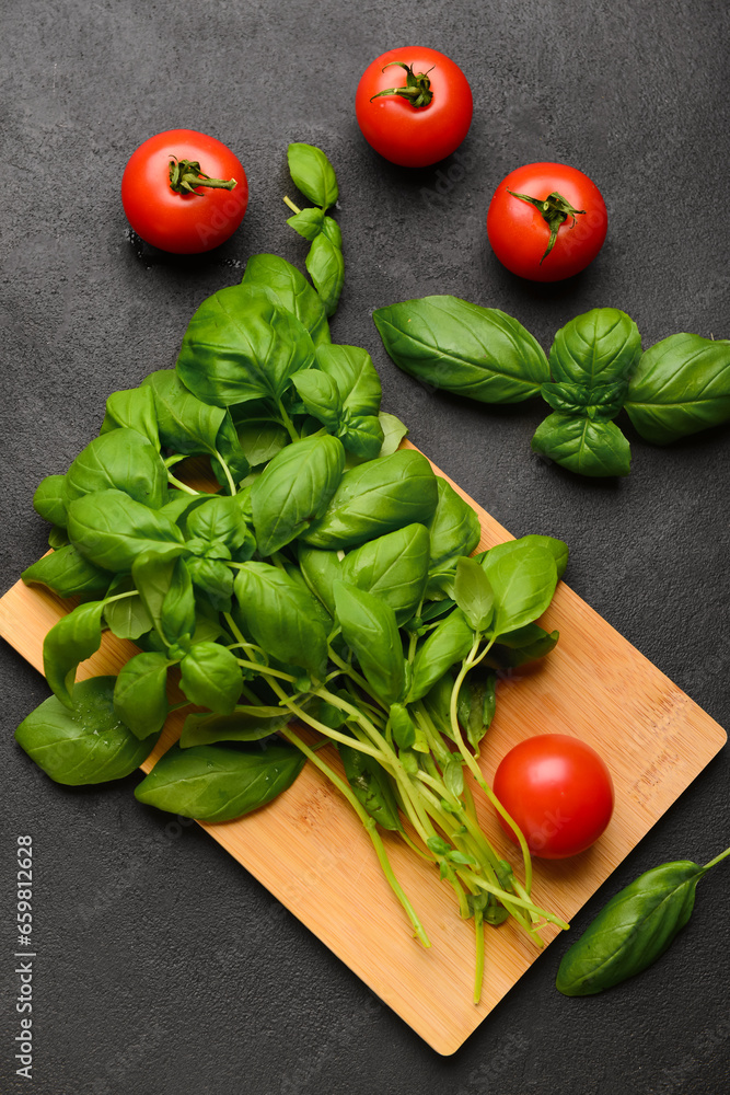 Wooden board with fresh green basil and tomatoes on black background