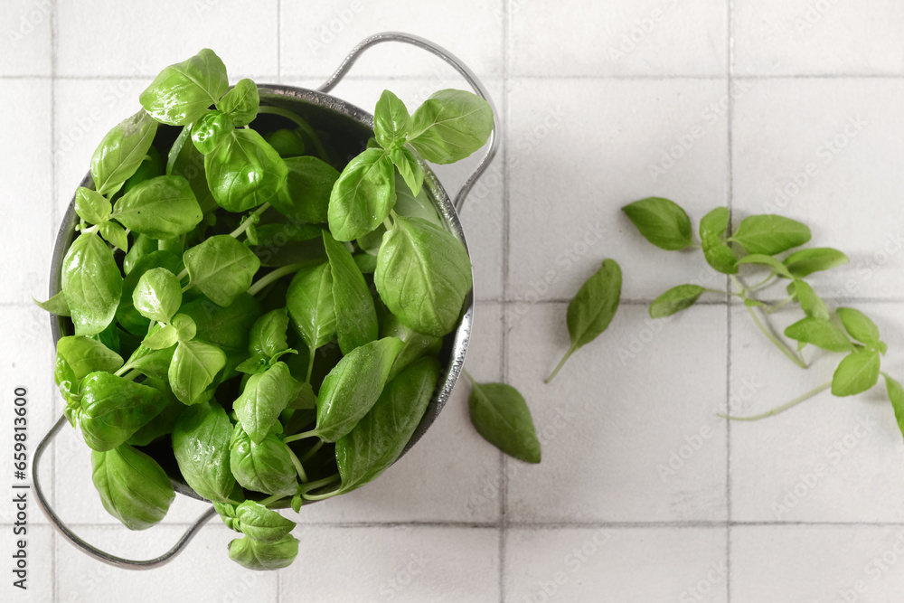 Cooking pot with fresh green basil on white tile background