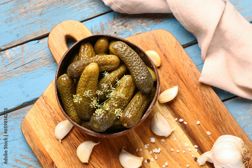 Bowl with tasty pickled cucumbers and different spices on blue wooden background