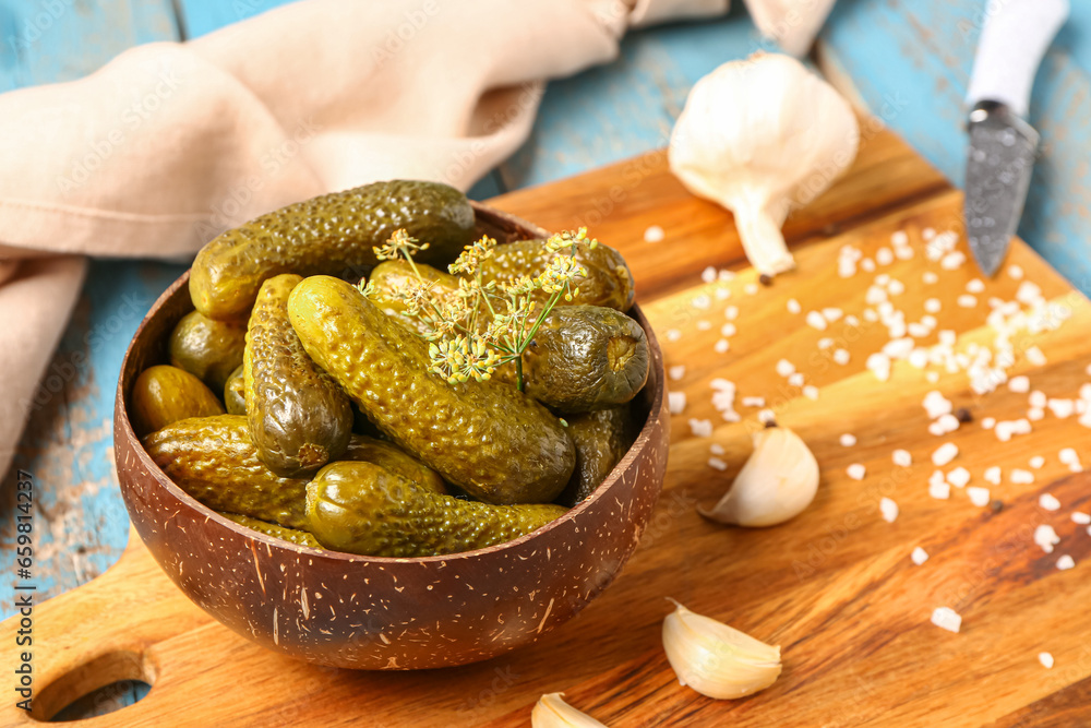 Bowl with tasty pickled cucumbers and different spices on blue wooden background