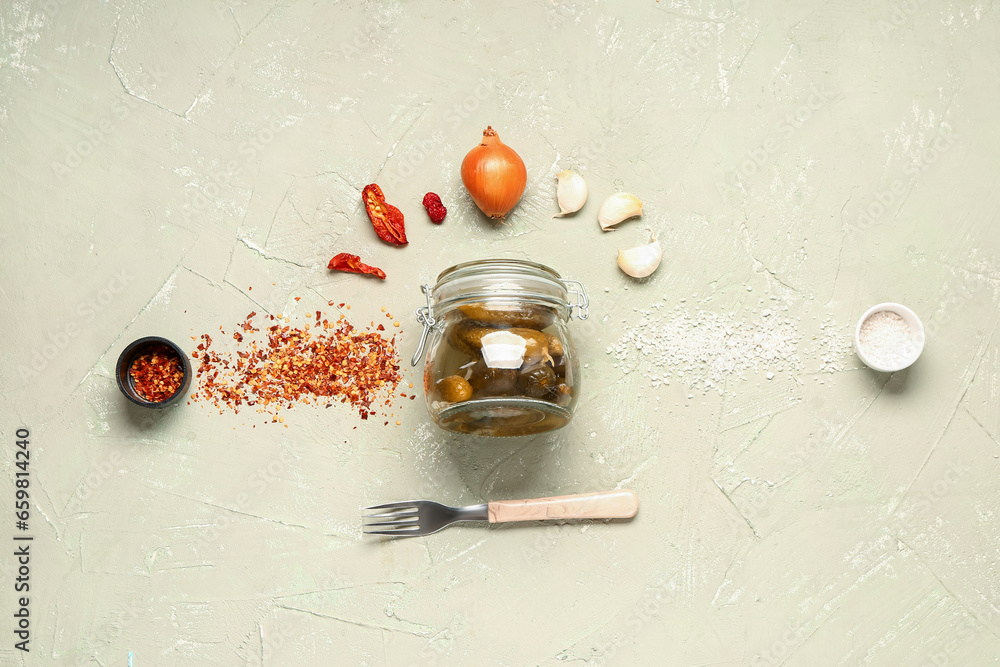 Jar with tasty pickled cucumbers and different spices on green background