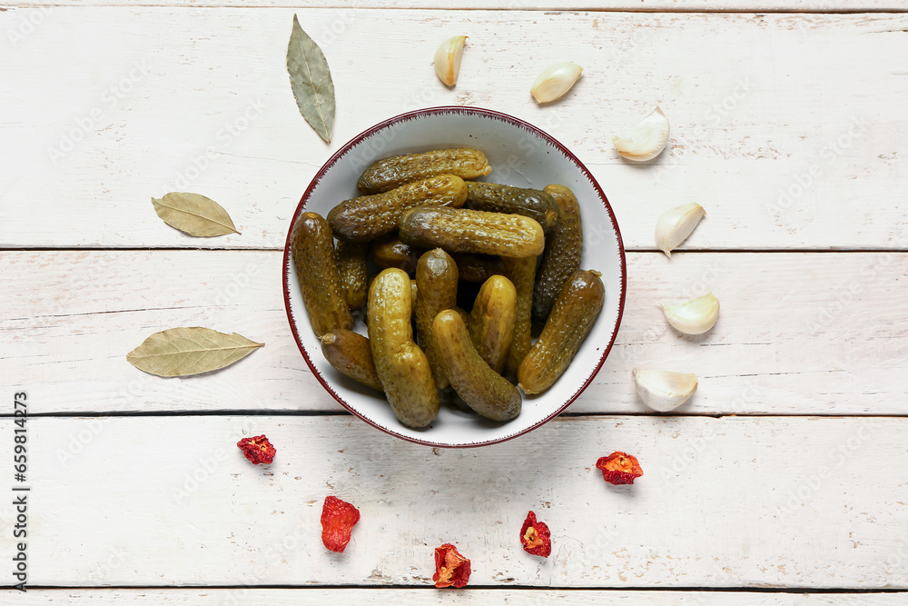 Bowl with tasty pickled cucumbers and different spices on white wooden background