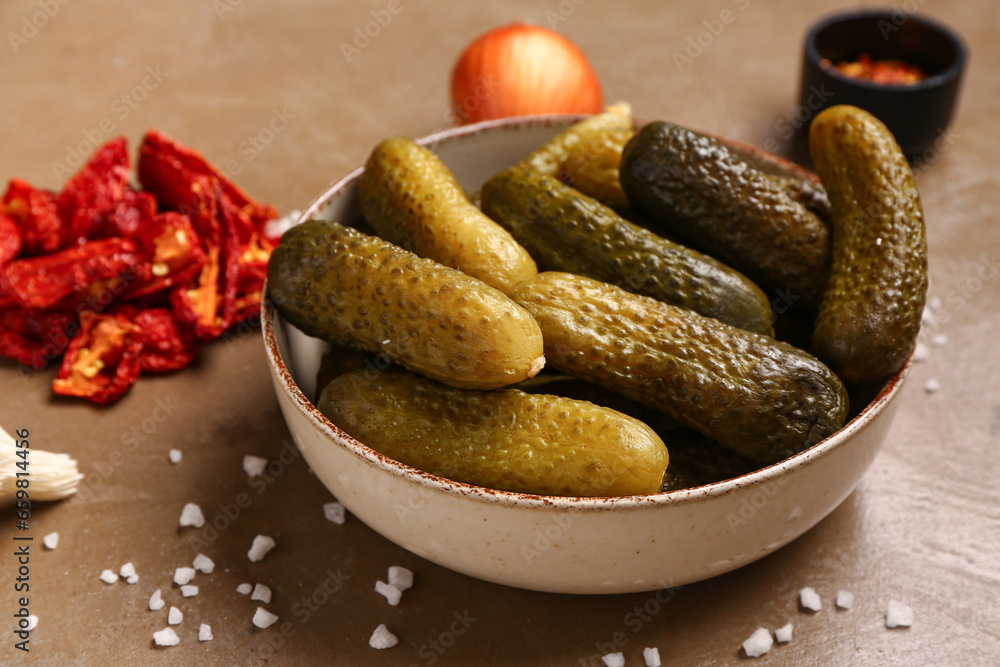 Bowl with tasty pickled cucumbers and different spices on brown background