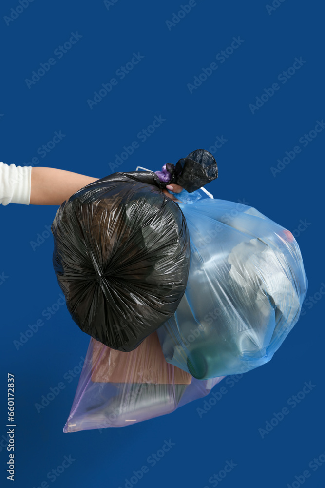 Female hand holding full garbage bags on blue background