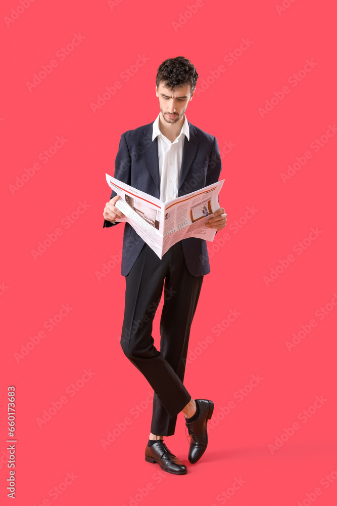 Young man in suit reading newspaper on red background