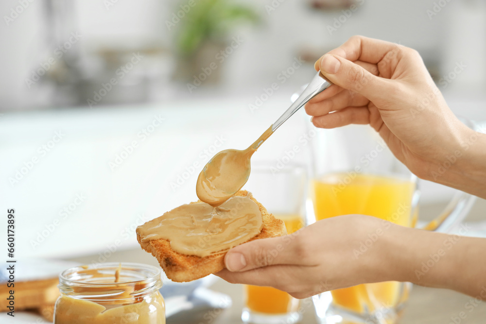 Young woman spreading nut butter onto toast in kitchen, closeup