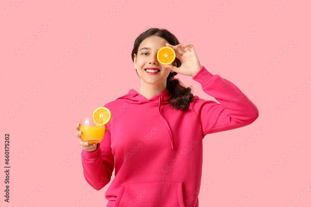 Teenage girl with glass of juice and orange on pink background