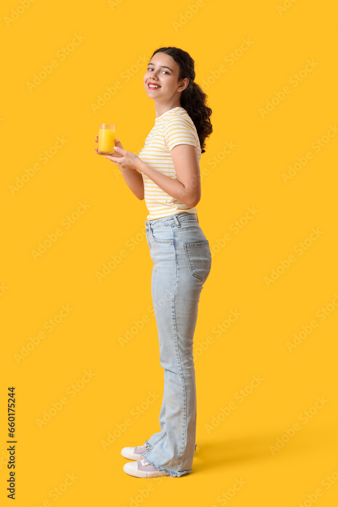 Teenage girl with glass of orange juice on yellow background