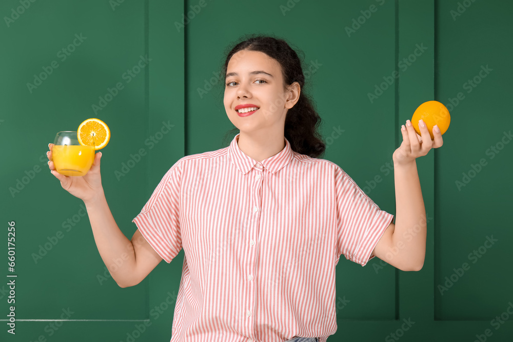 Teenage girl with glass of juice and orange on green background