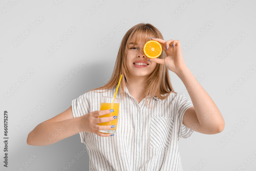 Teenage girl with glass of juice and orange on light background