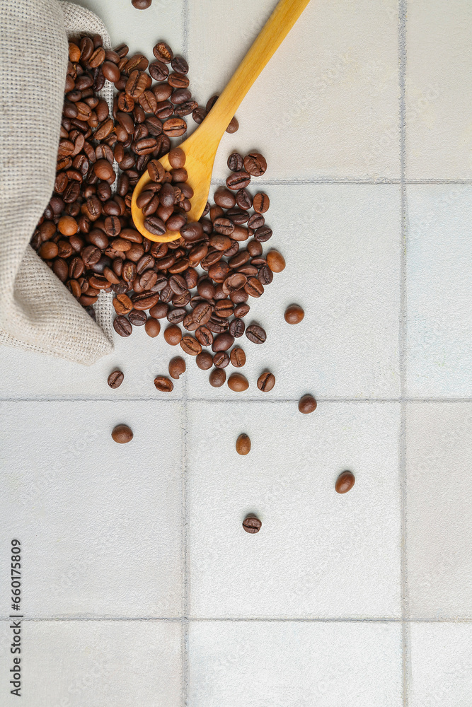 Scattered coffee beans with wooden spoon on light tile background