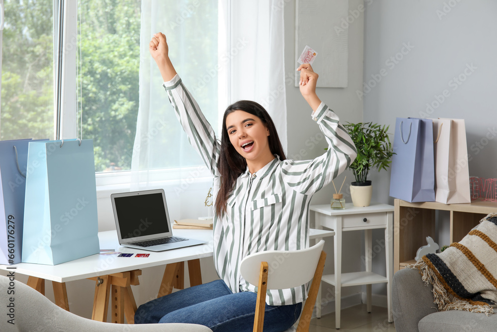 Happy young woman with gift card and laptop shopping online at home