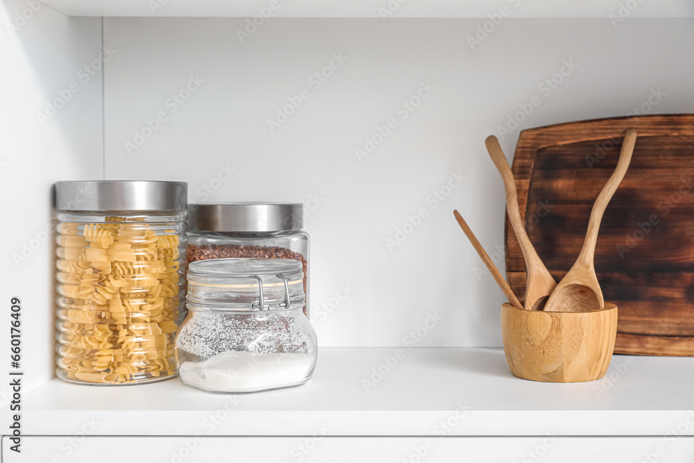 White shelf with cutting board, wooden spoons and jars