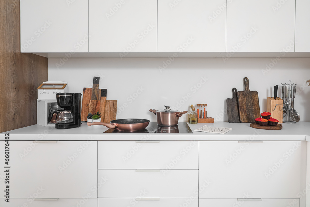 White kitchen countertop with electric stove, frying pan, cooking pot and utensils