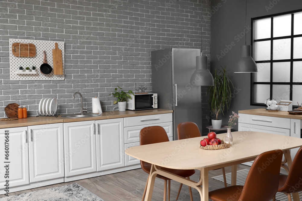 Interior of modern kitchen with white counters, dining table and fridge