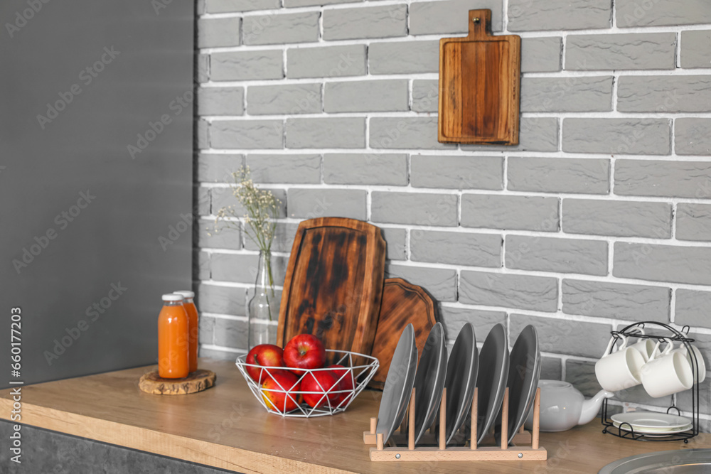 Wooden countertop with apples, plate rack and bottles of juice in modern kitchen