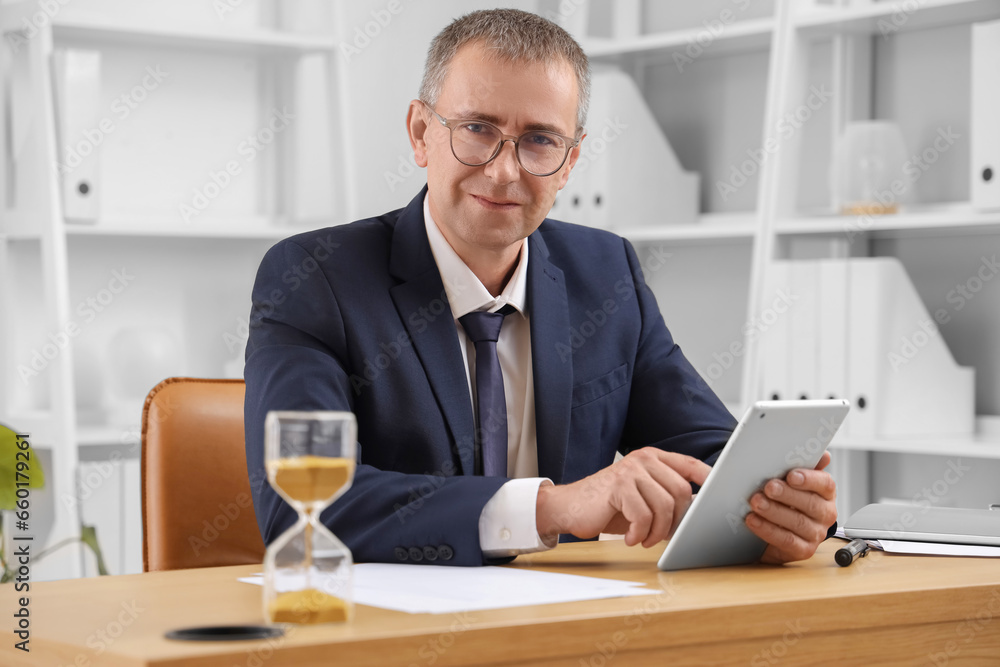 Mature businessman with tablet computer and hourglass in office