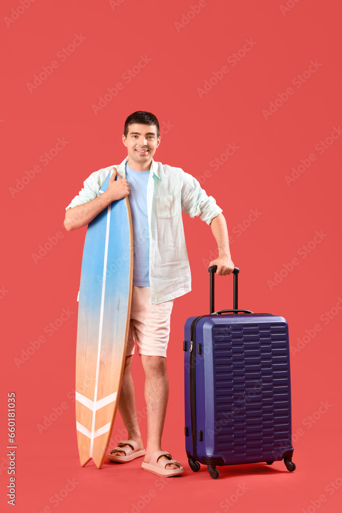 Male tourist with suitcase and surfboard on red background