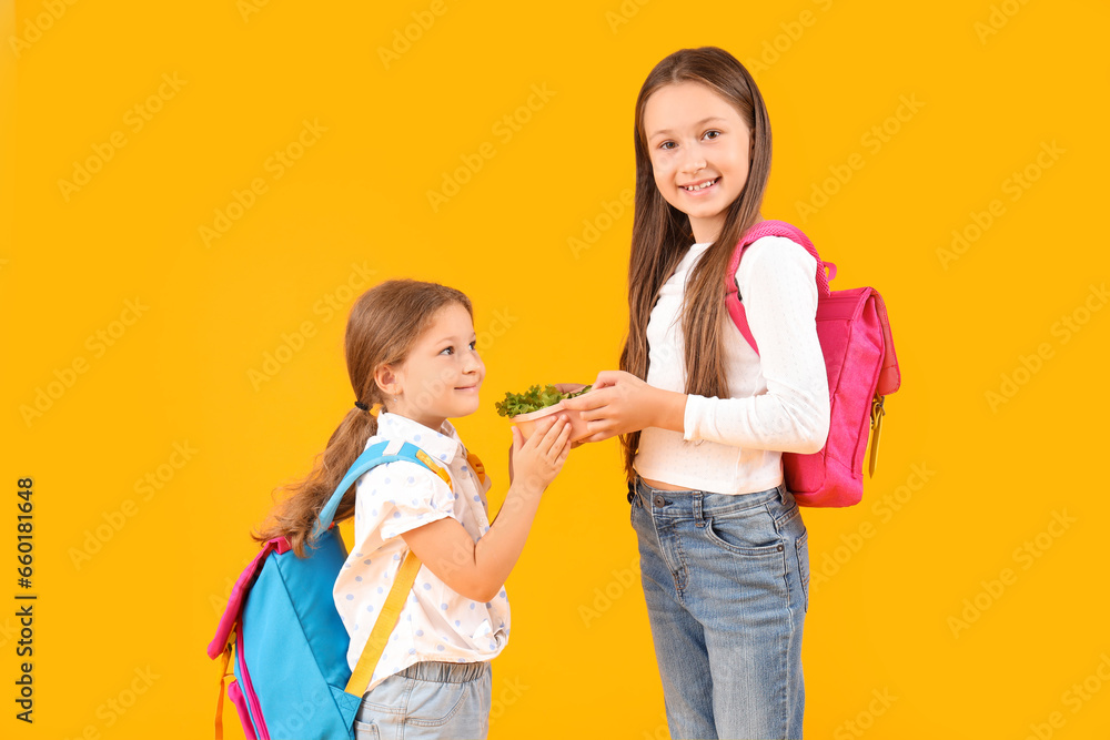 Happy girls with backpacks and lunchbox on yellow background