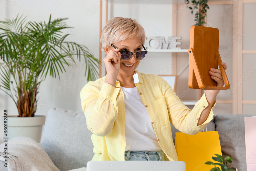 Mature woman with new sunglasses and mirror at home. Online shopping