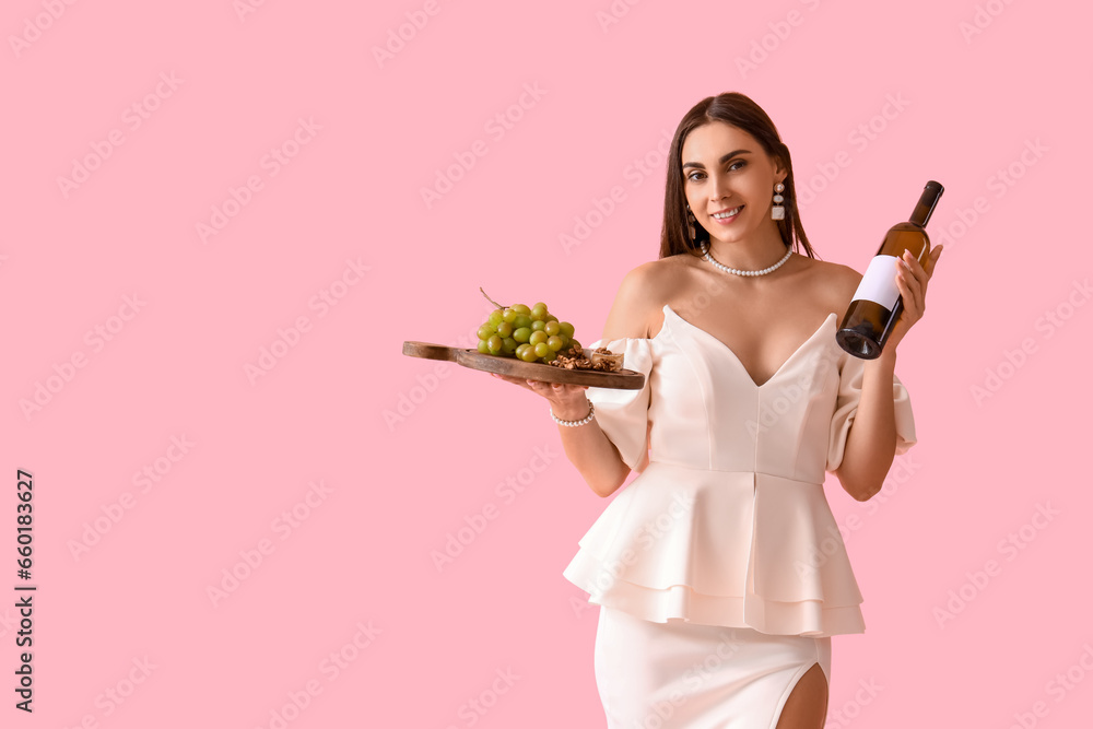 Young woman with bottle of wine and snacks on pink background