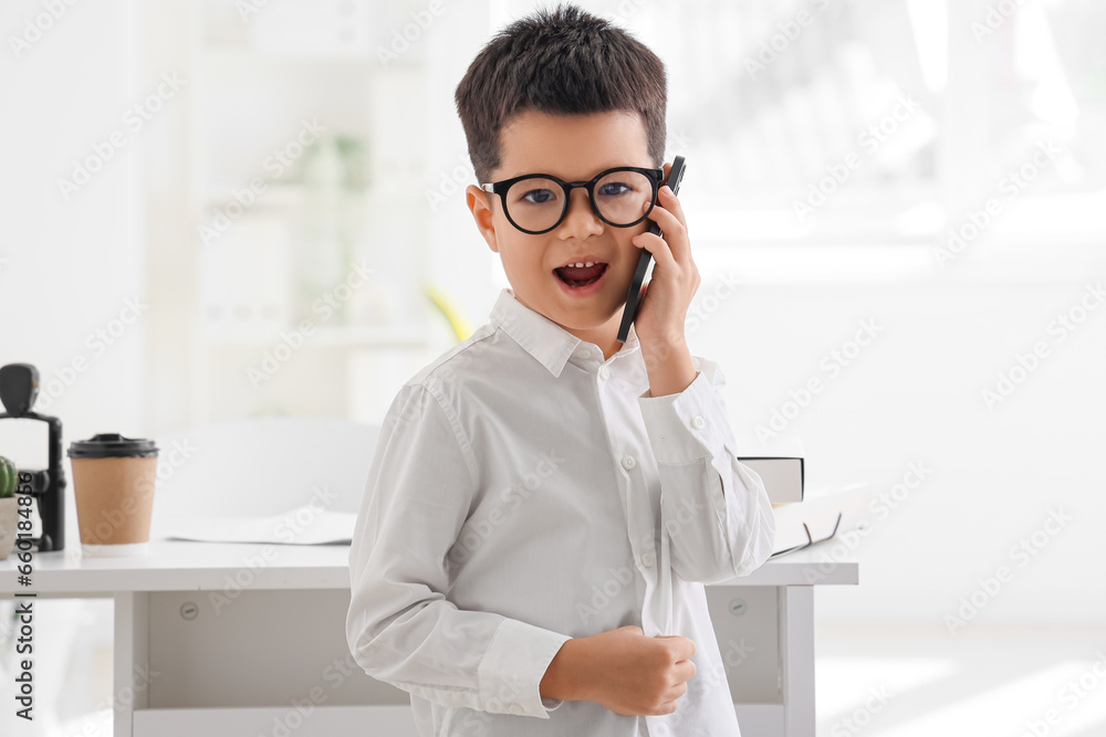 Cute little businessman talking by mobile phone in office