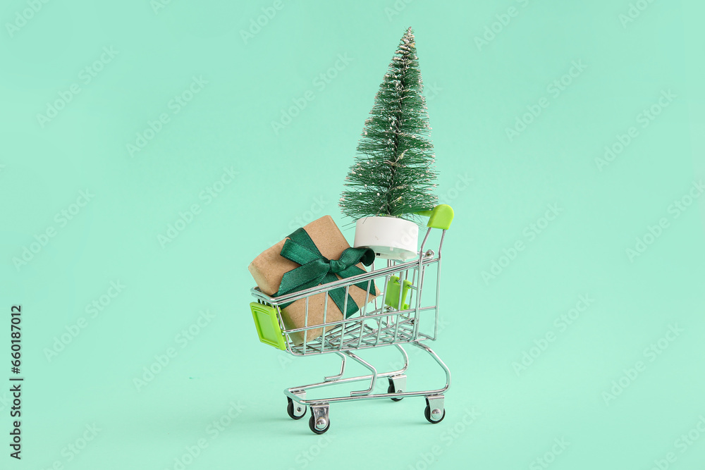 Shopping cart with Christmas tree and gift box on green background