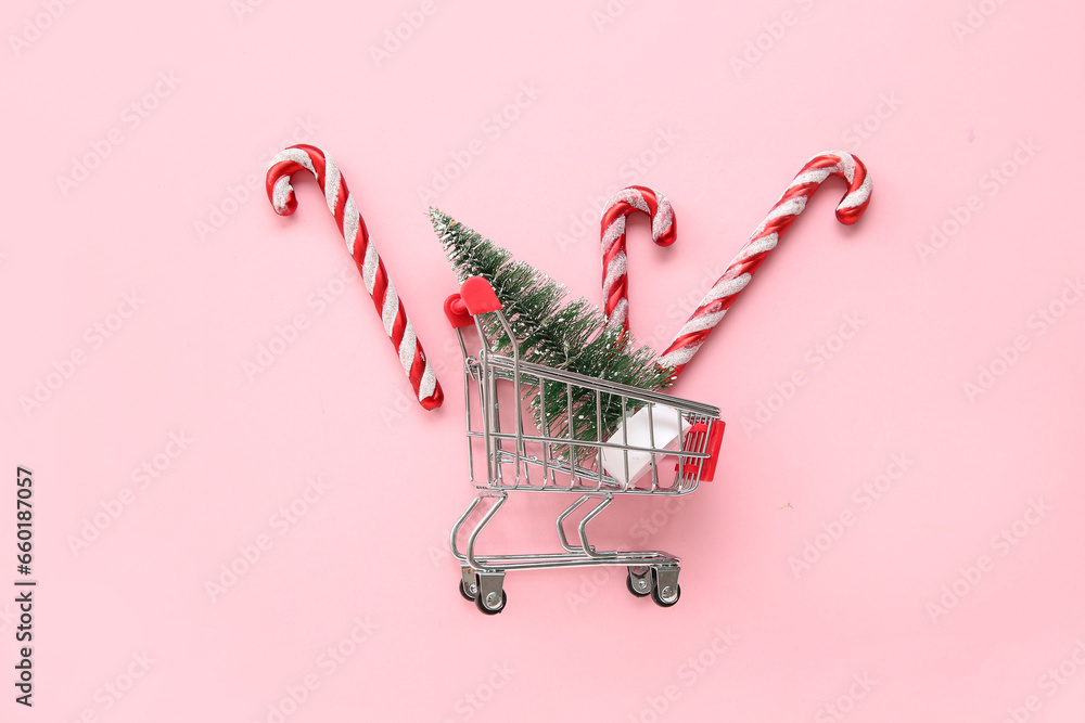 Shopping cart with Christmas tree and candy cane toys on pink background