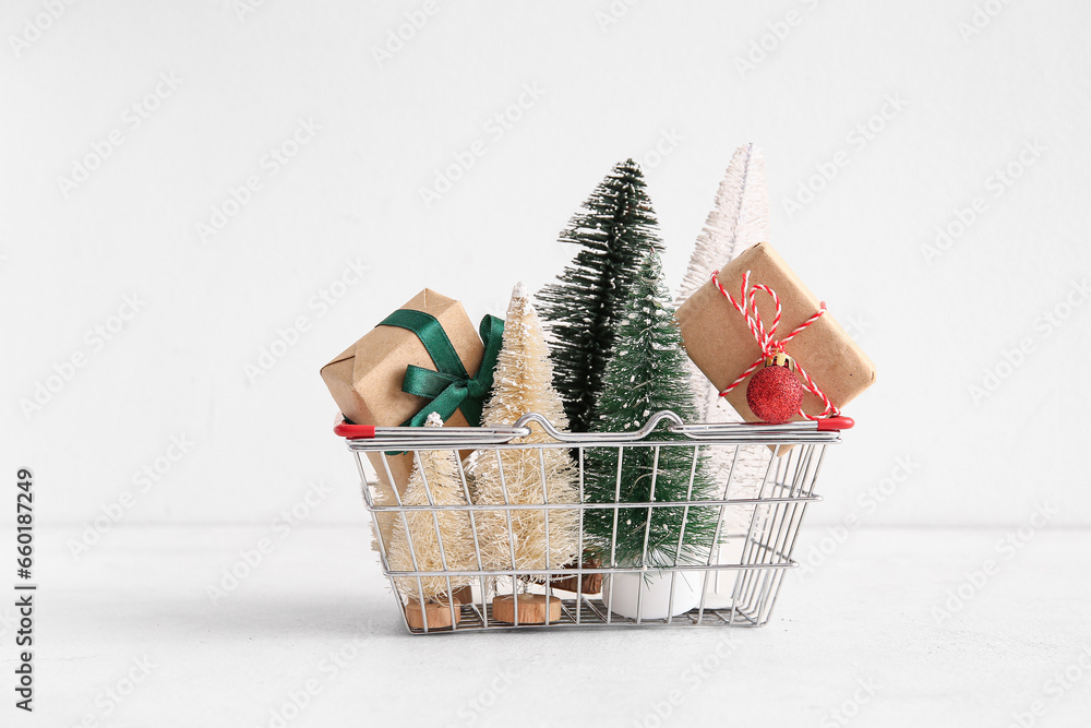 Shopping basket with Christmas trees and gift boxes on white background