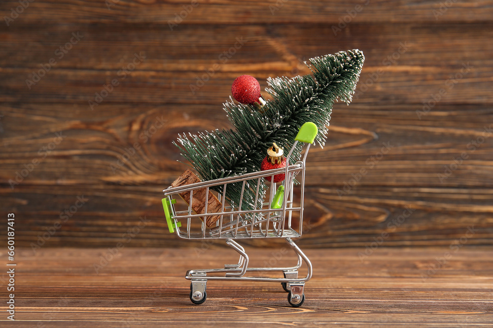 Shopping cart with Christmas tree and balls on wooden background