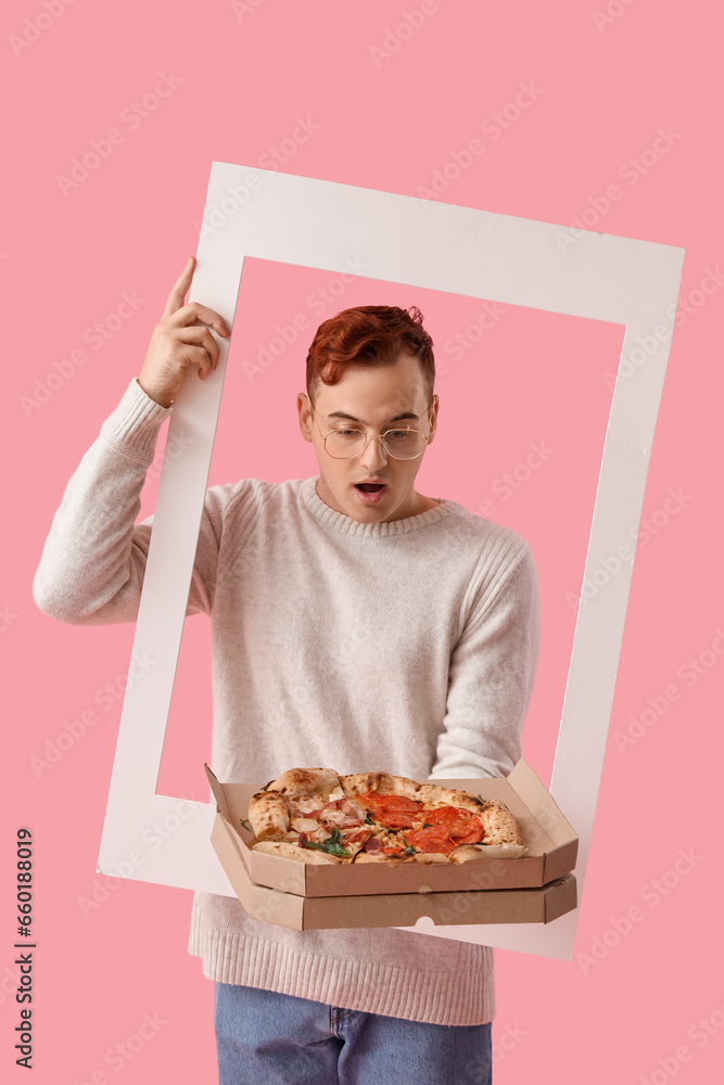 Surprised young man with tasty pizza and frame on pink background