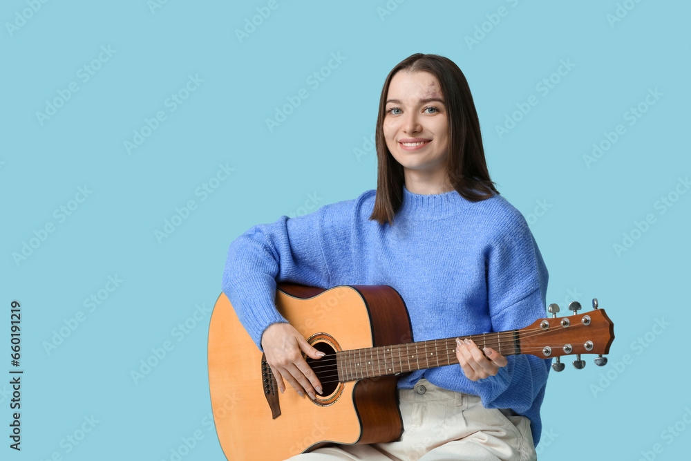 Pretty young woman playing acoustic guitar on blue background