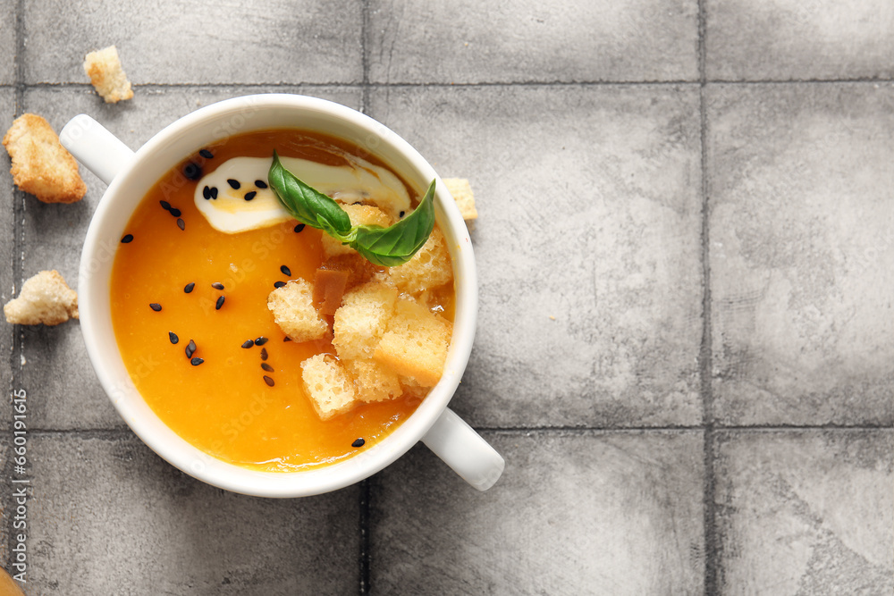 Pot of delicious pumpkin cream soup with croutons and basil on grey tile background