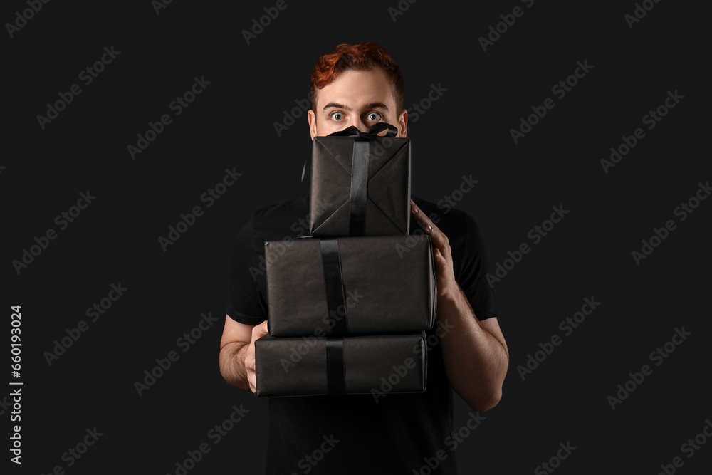 Young man with gift boxes on dark background. Black Friday sale