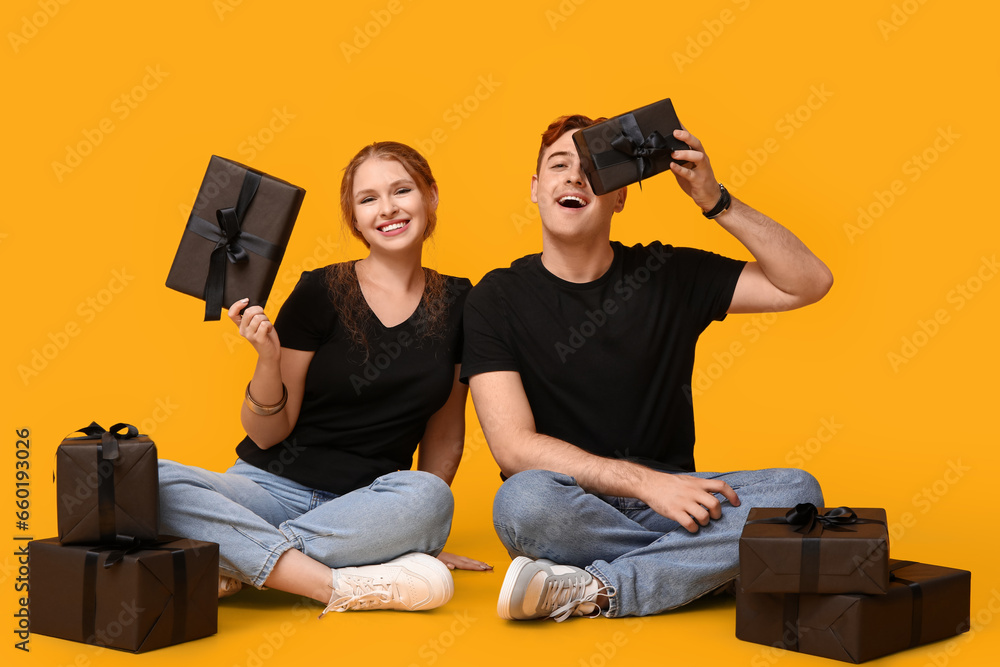 Young couple with gift boxes sitting on yellow background. Black Friday sale