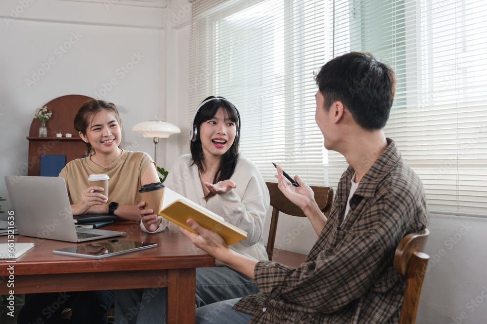 A group of cheerful Asian college students are enjoying talking and discussing their group project while sitting in a coffee shop together.