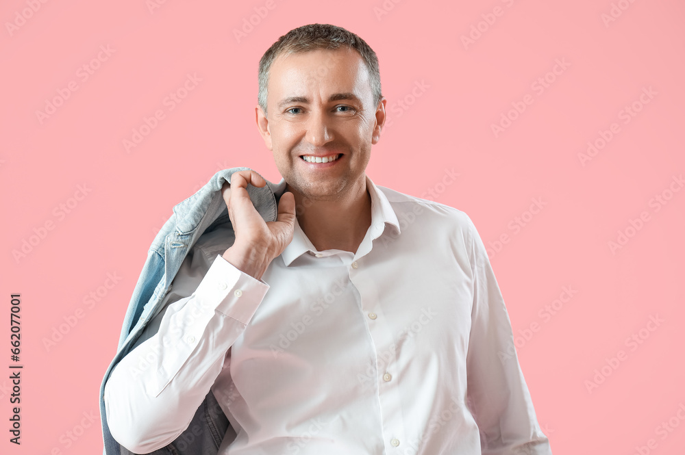 Portrait of happy mature man with denim jacket on shoulder against pink background