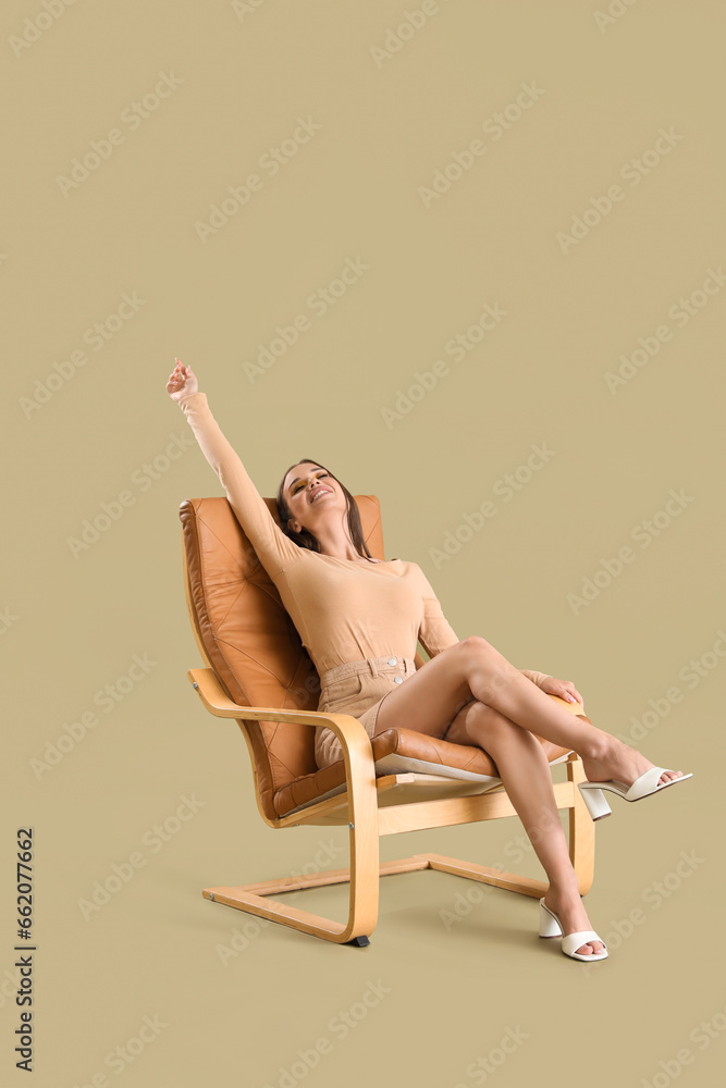 Beautiful happy young woman sitting on comfortable modern chair against green background