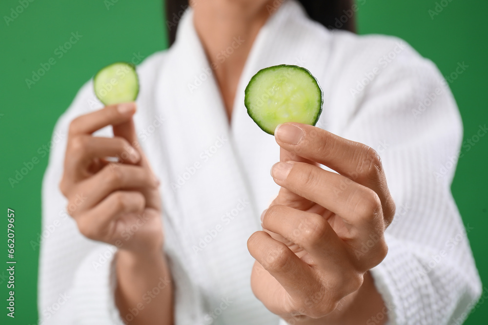 Young woman with cucumber slices on green background, closeup