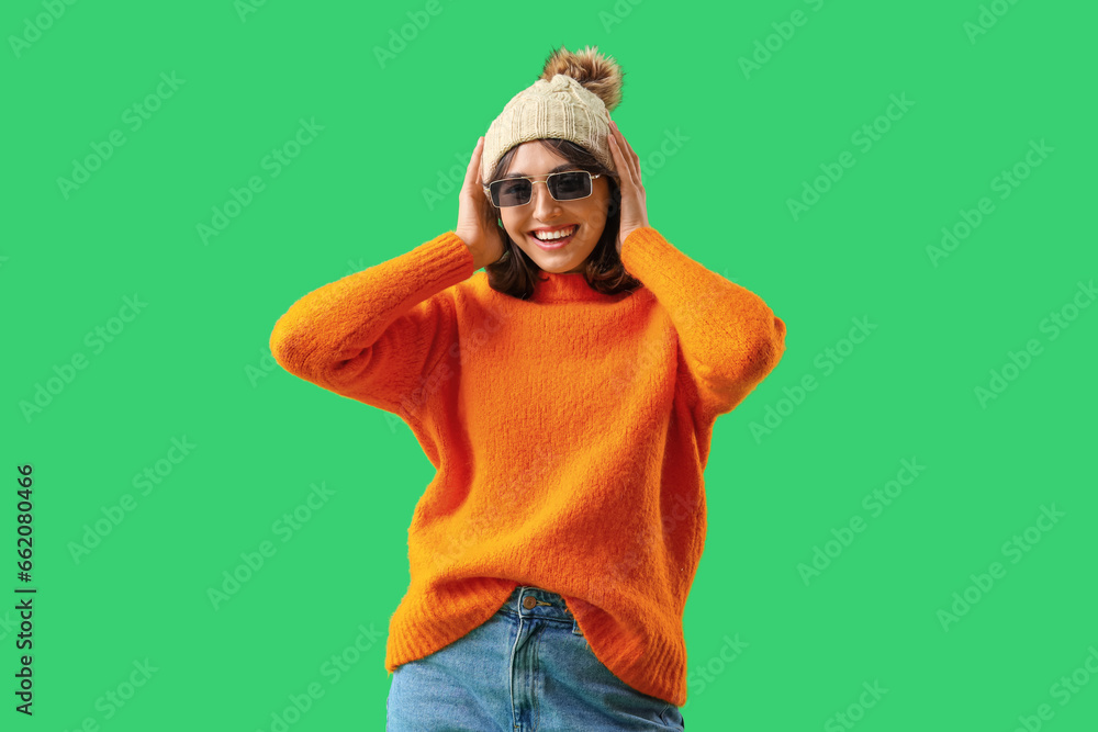 Young woman in warm clothes with sunglasses on green background