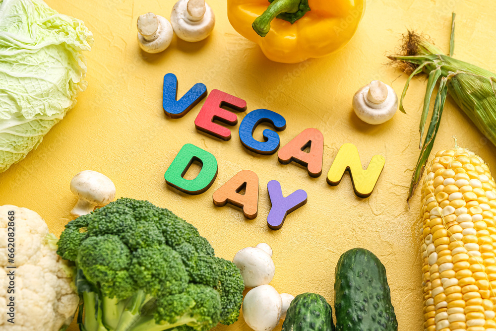 Text VEGAN DAY and different fresh vegetables on yellow background